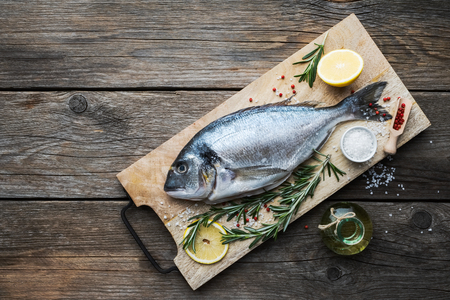 Fresh dorado fish with lemon slices,  sea salt and rosemary twigs on wooden cutting board. Top view. Copy space for text.