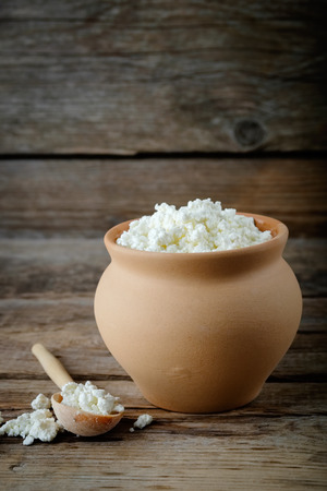 Cottage cheese in brown rustic clay pot and wooden spoon.の写真素材