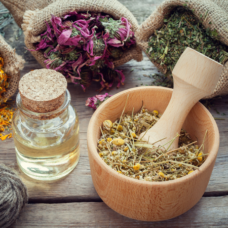 Medicinal herbs in hessian bags, wooden mortar of dry chamomile buds and essential oil on wooden table, herbal medicine.の写真素材