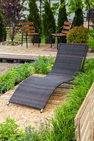 A place to relaxation at backyard in garden: lounge chair, wooden chairs, flowerbed and beautiful...