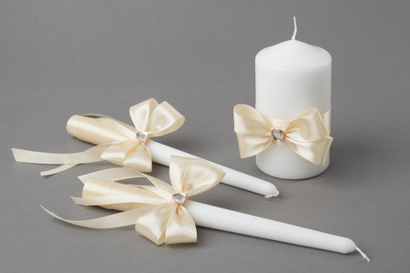 Three candles decorated with beige silk bows on grayの写真素材