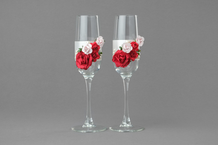 Two ornate wedding wine glasses decorated with red and pink roses on grayの写真素材