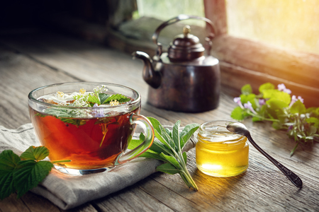 Several medicinal plants and herbs on table, healthy herbal tea cup, honey jar and vintage copper tea kettle.の写真素材