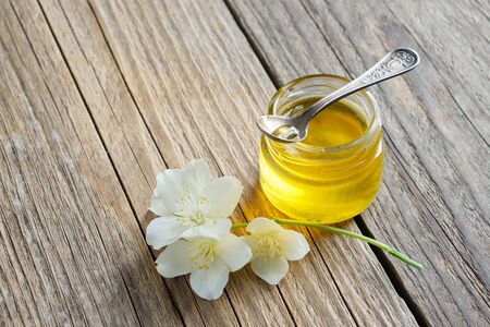 Small honey jar and Philadelphus or garden jasmine flowers on wooden board.の写真素材