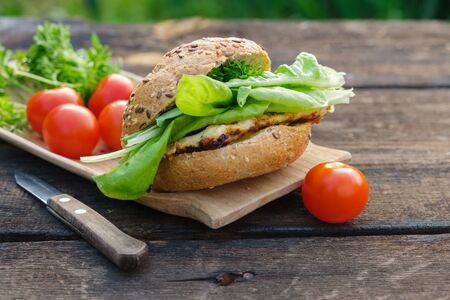Tasty homemade burger and lettuce, tomatoes on wooden picnic table outdoors.の写真素材