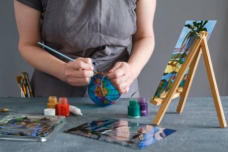 Painter holding a paintbrush in his hand and painting with stained glass paints on a glass vase.の写真素材