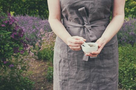 Woman holding in her hands a mortar of healing herbs. Herbalist collects medicinal plants in garden.の写真素材