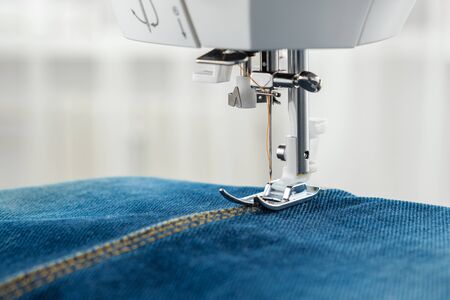 Sewing denim jeans with sewing machine. Close up of needle of sewing machine on the denim fabric...