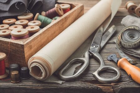 Sewing items: retro tailoring scissors, measuring tape, thimble, vintage spools of thread in wooden box, patterns on paper and tailor cutting knife.の写真素材