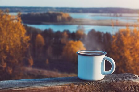Enameled cup of coffee or tea on autumn landscape outdoors.の写真素材