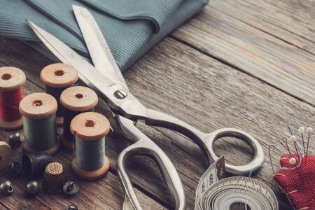 Retro sewing items: tailoring scissors, cutting knife, thimble, wooden thread spools, cushion for including pins, fabrics and sewing accessories.の写真素材