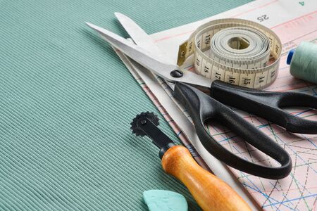 Sewing tailor items: scissors, measuring tape, spool of thread, patterns on paper, seamstress cutting knife, chalk on green jersey knitted fabrics.の写真素材
