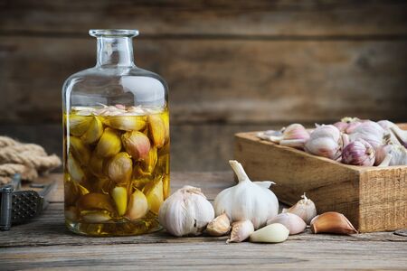 Garlic aromatic flavored oil or infusion bottle, wooden crate of garlic cloves and  garlic press on wooden kitchen table.の写真素材