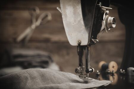 Old antique sewing machine with  linen cloth. In the background is a hanging tailoring scissors. Retro tailor workshop.の写真素材