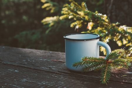 Enameled cup of coffee or tea on wooden board in summer forest outdoors.の写真素材