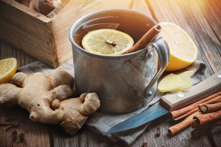 Ginger tea cup with lemon and cinnamon, ginger roots, knife and cinnamon sticks on kitchen table. の写真素材