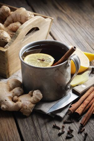 Ginger tea cup with lemon and cinnamon, ginger roots and cinnamon sticks on kitchen table. の写真素材