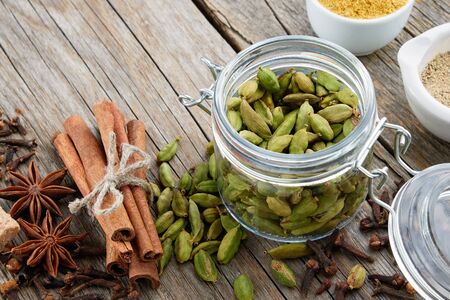 Jar of whole green cardamom pods and spices - cinnamon sticks, cardamom, allspices and anise on wooden table. Ayurveda treatments. の写真素材