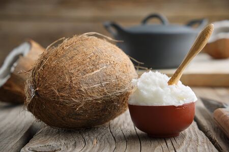 Healthy coconut oil for cooking in ceramic bowl and coconuts on wooden kitchen table.の写真素材