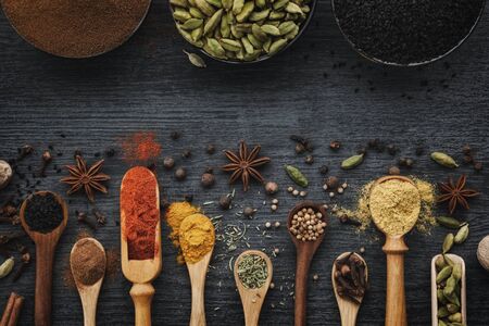 Various aromatic colorful spices and herbs in wooden spoons and scoops. Black ceramic bowls of seasonings. Ingredients for cooking.  Ayurveda treatments. Top view.の写真素材