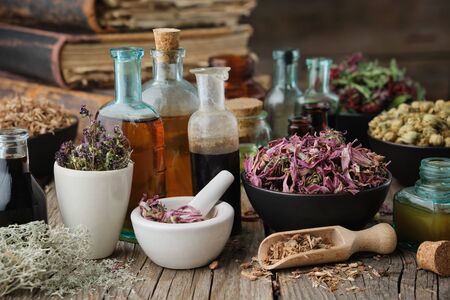 Bottles of healthy tincture or infusion, mortar and bowls of medicinal herbs, old books on wooden table. Herbal medicine.の写真素材