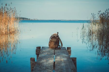 Backpack of traveller on wooden pier on blue summer lake.