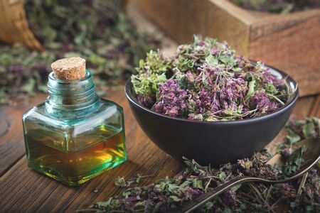 Bowl of dry Origanum vulgare or wild marjoram flowers. Bottle of essential oil or infusion.の写真素材
