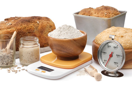 Homemade sourdough bread, natural leaven for bread in a glass jar, wooden bowl of dough, kitchen scale, a bowl of flour and oven thermometer on white.の写真素材