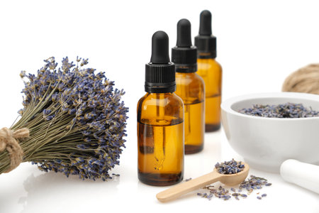 Dropper bottles of lavender essential oil or aromatic flower water, mortar, wooden spoon and bunch of dried lavender flowers on white.の写真素材