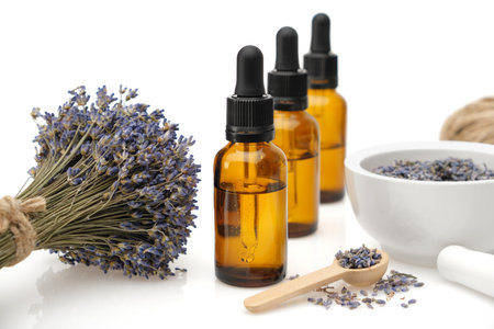 Three ropper bottles of lavender essential oil or aromatic flower water, mortar and bunch of dried lavender flowers on white background.の写真素材