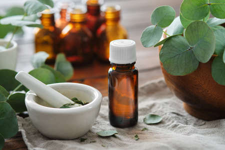Bottle of eucalyptus oil, mortar and wooden bowl of green eucalyptus leaves. Tincture and oil bottles on background, not in focus.の写真素材
