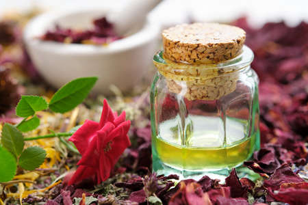 Essential oil bottle, rose flower and dried rose petals.