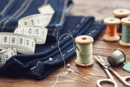 Shortening jeans. Measuring tape, scissors, spools of thread, thimble, including pins and chalk on...