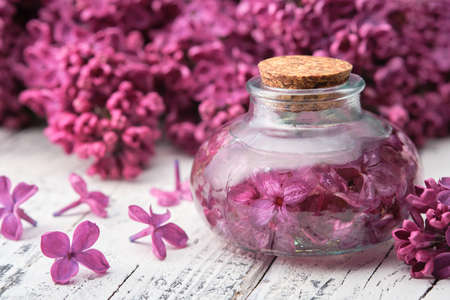 Bottle of oil or infusion from lilac flowers on white wooden table.の写真素材