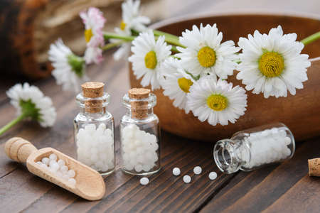 Bottles of homeopathy granules. Homeopathic remedy - Chamomilla. Daisies flowers in wooden bowl....