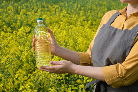 A woman stands in a rape field and holds a bottle of rapeseed oil in his hands. Concept of canola oil production.の写真素材