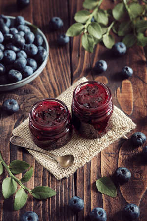 Two small jars of blueberry jam, blue plate of fresh blueberries on kitchen table.の写真素材