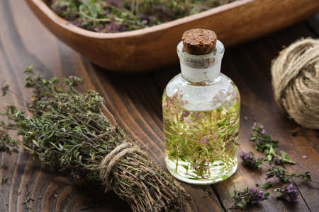 Bottle of thyme essential oil or infusion, bunch of dried thymus serpyllum plants and wooden crate filled with dry healthy thyme flowers on wooden table. Alternative medicine.の写真素材