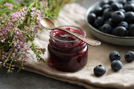 Small jar of blueberry jam and plate of fresh ripe blueberries on kitchen table.の写真素材