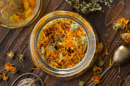 Glass jar of dried calendula flowers, cup of healthy calendula herbal tea, thyme medicinal herbs on wooden table. Top view. Alternative herbal medicine.の写真素材