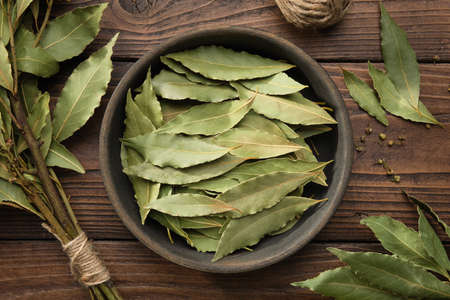 Bowl of dried laurel leaves. Branch of green bay leaves on wooden table, top view.の写真素材