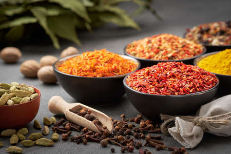 Bowls of various aromatic spices and herbs. Different seasoning - red hot pepper, paprika, anise, saffron, nutmegs, cardamom pods,  gloves, curcuma, laurel leaves. Condiments for healthy cooking.の写真素材