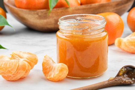 Jar of healthy tangerine jam on white kitchen table. Wooden bowl of tangerine oranges fruit on background.の写真素材