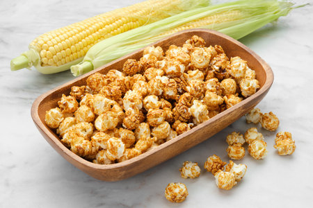 Wooden bowl of caramel popcorn, fresh corncobs on background.の写真素材