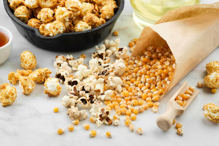 Prepared popcorn in a frying pan, dried corn grains, caramel sauce and oil bottle on kitchen table.の写真素材