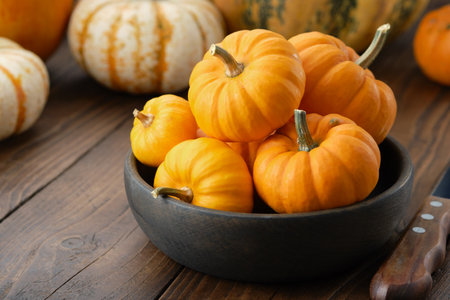 Several small pumpkins in a wooden bowl on a kitchen table.の写真素材