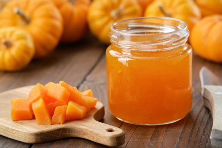 Jar of healthy pumpkin jam. Chopped pumpkin pulp on a cutting board. Pumpkins in the background.の写真素材