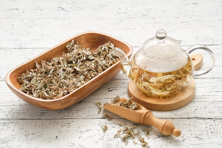 Glass teapot of herbal Icelandic moss tea. Wooden scoop and bowl dried of Iceland moss on white table. Cetraria islandica - latin name of plant. alternative herbal medicine.の写真素材
