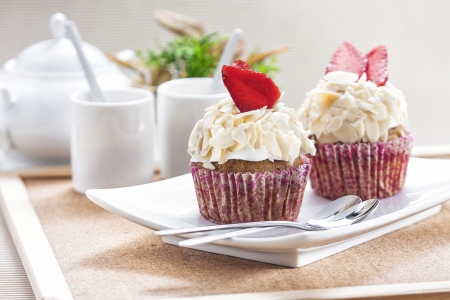 Vanilla cupcake with strawberry and almond against tea set in wooden frame on brown corrugated background  の写真素材