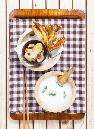Gruel with hot and sour  pickle against fried dried fish on wooden background      の写真素材